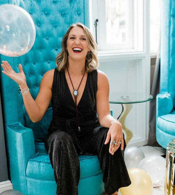 Woman sitting in tall velvet chair playing with clear balloon