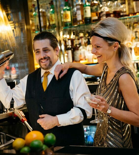 two bartenders mixing drinks while wearing old hollywood costumes