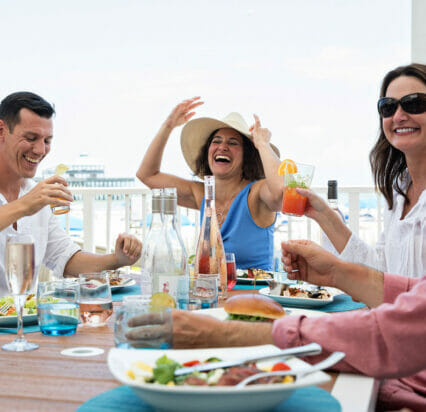 friends gathered around outdoor dining table next to waterfront